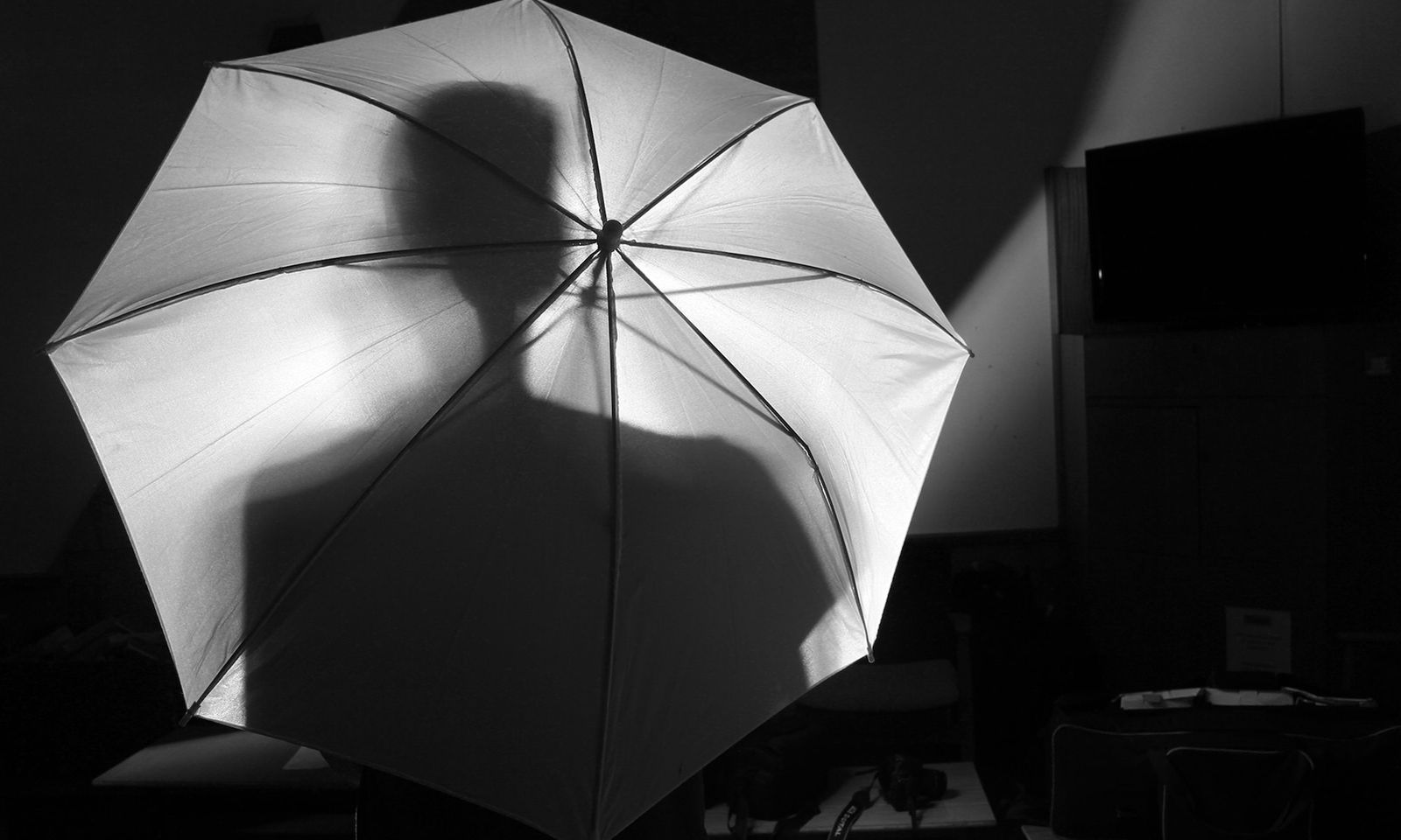 A dark room with a silhouette of a person behind an umbrella 