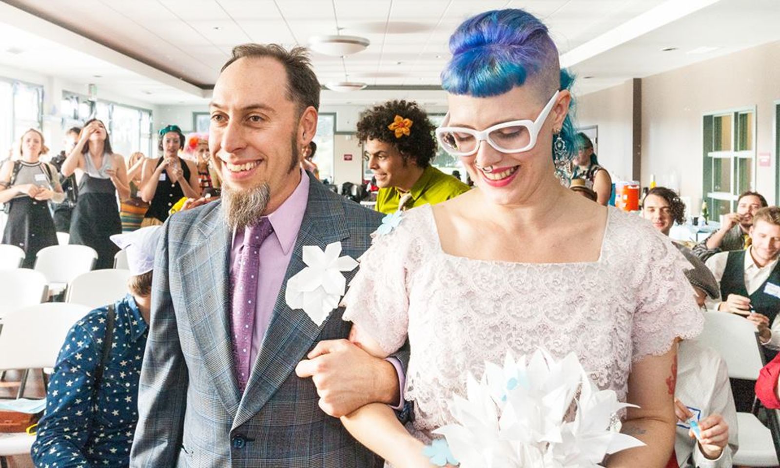 My partner and I walking down the aisle arm in arm carrying a paper flower bouquet