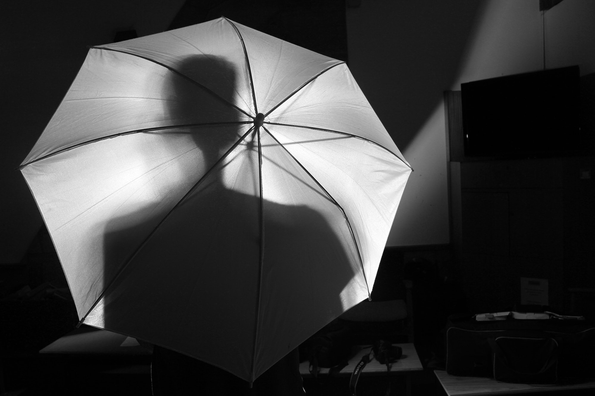A dark room with a silhouette of a person behind an umbrella 