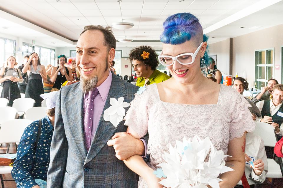My partner and I walking down the aisle arm in arm carrying a paper flower bouquet